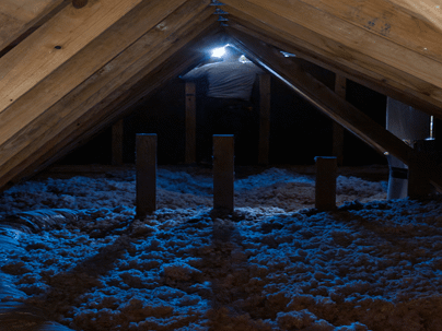 A technician illuminates an attic with his flashlight.